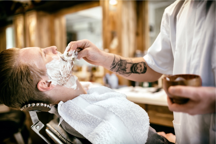 Barbeiro prepara cliente para tratamento de foliculite e remoção da barba.