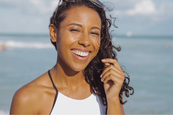 Mulher negra cuida de cabelo em piscina e praia.