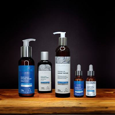 Imagem de um kit de produtos de cuidado masculino da linha Vita Hominis da Grandha, exibindo diversos itens como creme para pentear, gel de barbear e séruns em um fundo escuro.
