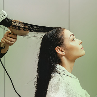 Mulher com cabelos molhados sendo escovados com secador; texto destaca como escolher um bom protetor térmico para os cabelos.