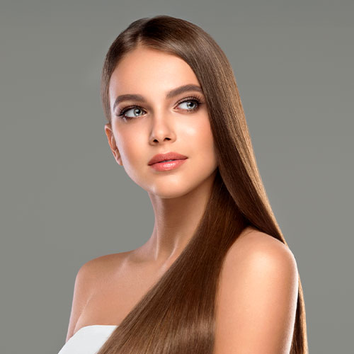 Mulher com cabelos longos, lisos e brilhantes, olhando para o lado com expressão serena em fundo cinza.