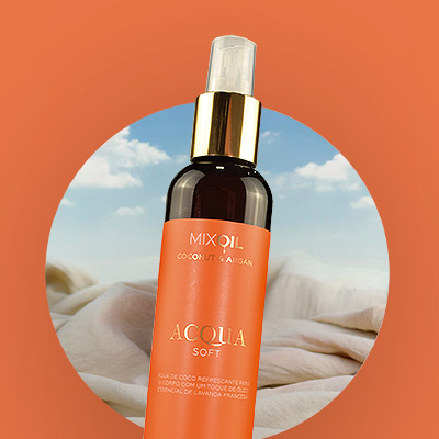 Frasco do Acqua Soft Mix Oil com óleo de coco e argan, posicionado em frente a um fundo com céu azul e nuvens, sobre tecido claro.