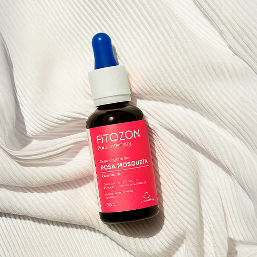 Frasco de óleo vegetal de rosa mosqueta Fitozon sobre tecido branco, com rótulo rosa e conta-gotas azul.