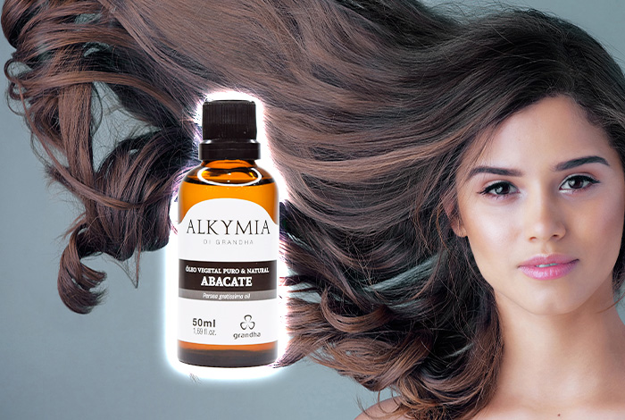 Pessoa com cabelos longos soltos ao vento ao lado de um frasco de óleo vegetal de abacate Alkymia di Grandha, usado para cuidados capilares.