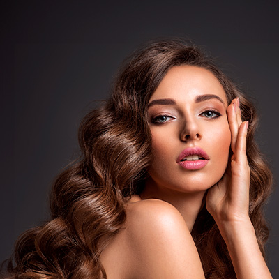 Mulher com cabelos longos e ondulados, destacando sua beleza e pele saudável, com expressão suave e elegante.