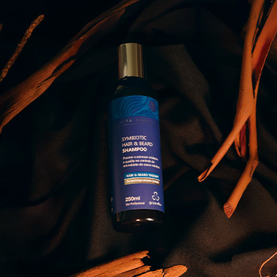 Imagem de um shampoo masculino para cabelo e barba em embalagem preta, fotografado sobre fundo escuro com detalhes de madeira ao redor.