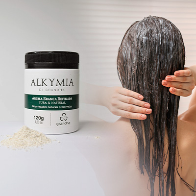 Produto Alkymia de Grandha com argila branca refinada ao lado de mulher aplicando o produto nos cabelos molhados, simbolizando cuidado capilar natural.