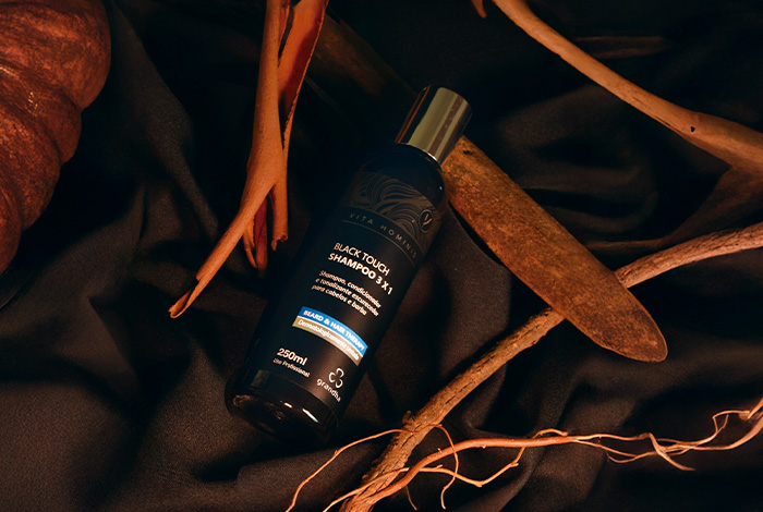 Frasco de shampoo preto masculino sobre tecido escuro, cercado por galhos e folhas secas, em cenário natural e sofisticado.