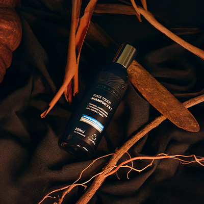 Frasco de shampoo preto masculino sobre tecido escuro, cercado por galhos e folhas secas, em cenário natural e sofisticado.