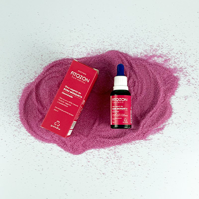 Frasco de óleo vegetal Fitozon Rosa Mosqueta da Grandha com caixa rosa, sobre fundo branco e areia rosa, em composição estética e natural.