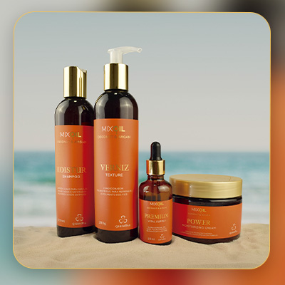 Conjunto de produtos Mix Oil Coconut & Argan sobre a areia, com o mar ao fundo, simbolizando hidratação intensa e cuidados capilares de verão.