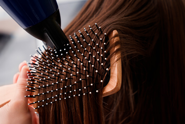 Como escolher um protetor térmico bom para seu tipo de fio? 1 Secador e escova modelando cabelo castanho, mostrando proteção térmica e cuidado durante a finalização dos fios.