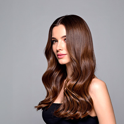 Mulher com cabelos longos, castanhos e brilhantes, exibindo fios alinhados e aspecto saudável sobre fundo neutro.