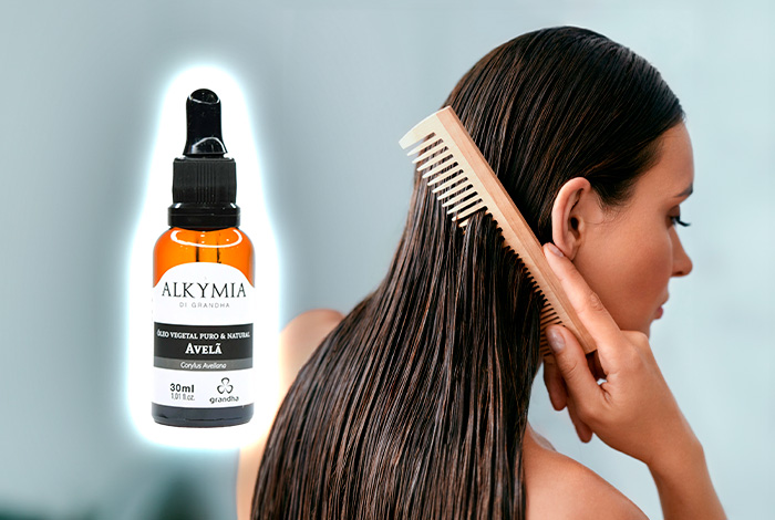 Mulher penteando o cabelo úmido ao lado de um frasco do Óleo Vegetal de Avelã Alkymia di Grandha em destaque.