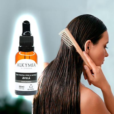 Mulher penteando o cabelo úmido ao lado de um frasco do Óleo Vegetal de Avelã Alkymia di Grandha em destaque.