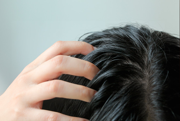 Pessoa tocando o couro cabeludo com fios escuros, destacando aspecto oleoso do cabelo próximo à raiz.