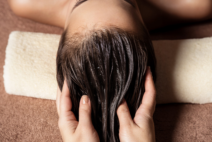 Pessoa recebendo massagem no couro cabeludo com óleo, destacando cuidado capilar e aplicação de óleo essencial de alecrim.