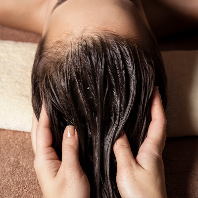 Pessoa recebendo massagem no couro cabeludo com óleo, destacando cuidado capilar e aplicação de óleo essencial de alecrim.