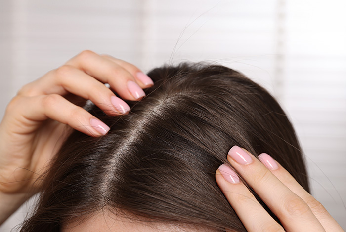 O que pode causar inflamação no couro cabeludo? 1 Pessoa examinando o couro cabeludo com as mãos, mostrando a raiz do cabelo e a linha de divisão dos fios.