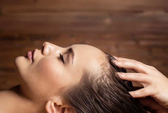Mulher relaxando durante massagem no couro cabeludo em ambiente de spa, com profissional aplicando técnica de cuidado capilar.