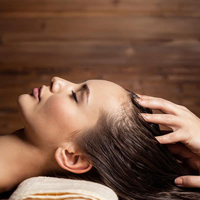 Mulher relaxando durante massagem no couro cabeludo em ambiente de spa, com profissional aplicando técnica de cuidado capilar.