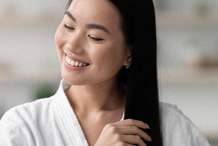 Mulher sorridente penteia os cabelos longos, cuidando dos fios em ambiente interno bem iluminado.