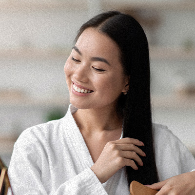Mulher sorridente penteia os cabelos longos, cuidando dos fios em ambiente interno bem iluminado.