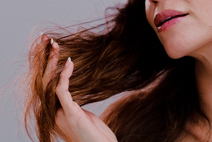 Pessoa segura mecha de cabelo ressecado, observando os fios, indicando danos ou fragilidade capilar.