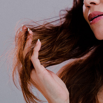 Pessoa segura mecha de cabelo ressecado, observando os fios, indicando danos ou fragilidade capilar.