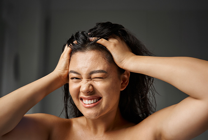 Couro cabeludo sensível: quais cuidados são importantes? 1 Mulher massageando o couro cabeludo com expressão de desconforto, representando coceira, sensibilidade e irritação no couro cabeludo.