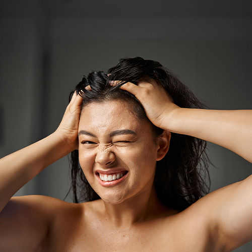 Mulher massageando o couro cabeludo com expressão de desconforto, representando coceira, sensibilidade e irritação no couro cabeludo.