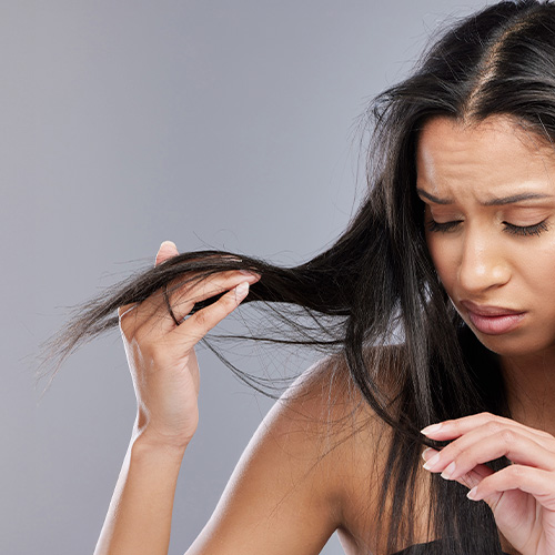 Mulher observando cabelo ressecado e pontas com frizz